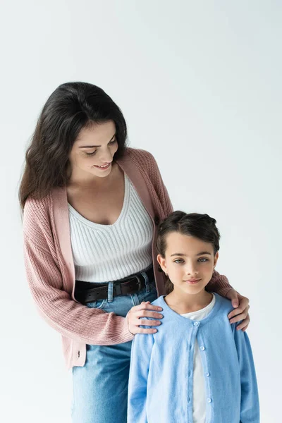 Young brunette woman embracing daughter and smiling isolated on grey — Foto stock