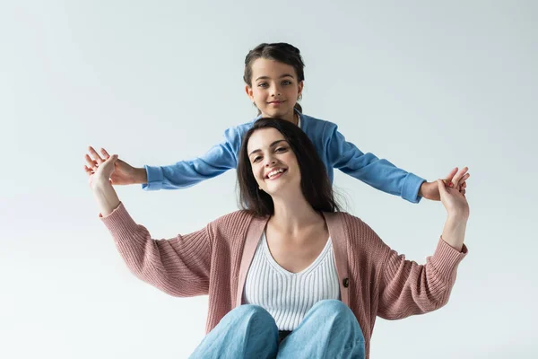 Cheerful mom and daughter holding hands and smiling at camera isolated on grey — Stockfoto