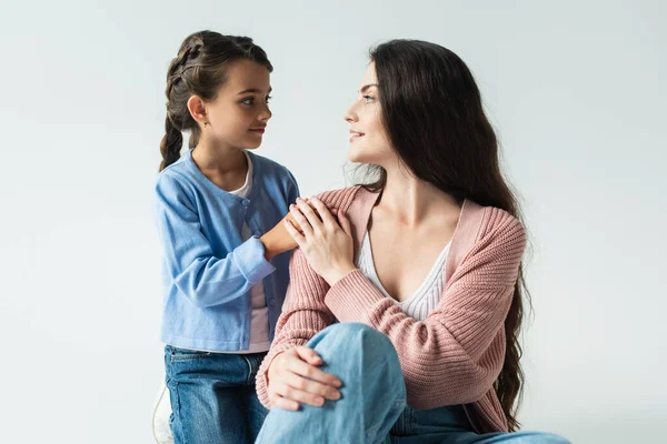 Brunette woman and smiling girl looking at each other isolated on grey - foto de stock