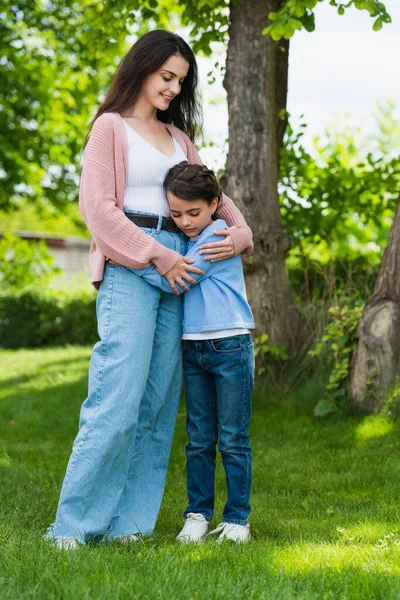 Задоволена жінка в джинсах обіймає дочку в парку — стокове фото