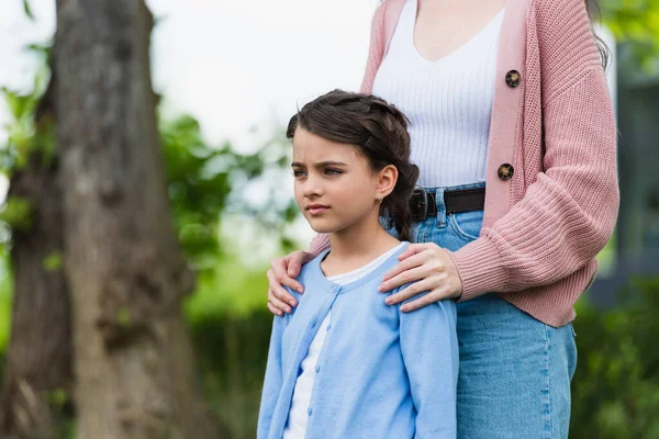 Woman hugging shoulders of thoughtful girl looking away outdoors - foto de stock