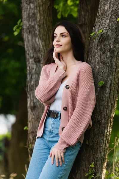 Dreamy and smiling woman touching face while looking away in park — Stock Photo