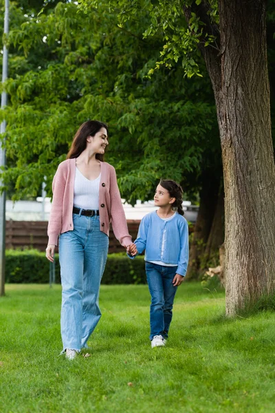 Happy woman and girl holding hands and looking at each other while walking in park — Stock Photo