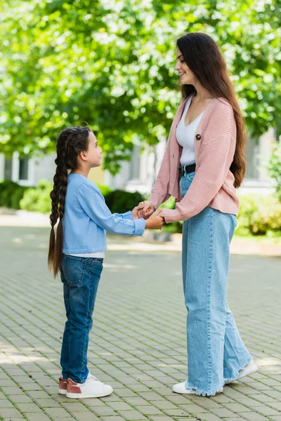 Side view of happy woman and child holding hands on urban street — стоковое фото