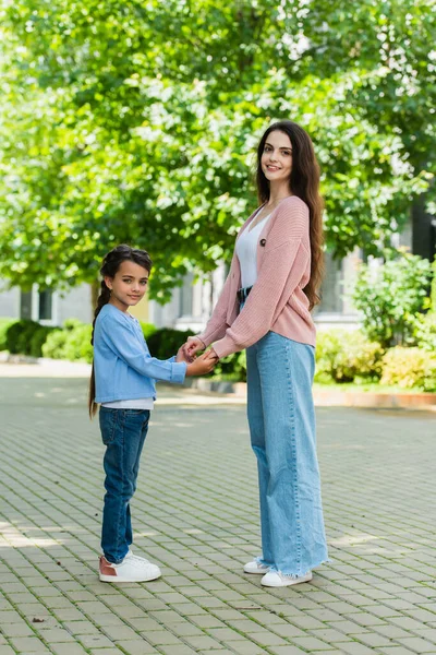 Happy mom and daughter holding hands and looking at camera on city street — Stock Photo