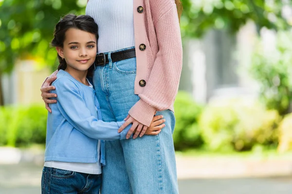 Smiling girl hugging mother and looking at camera outdoors — стоковое фото