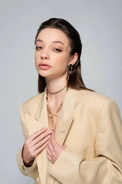 Young woman in beige blazer posing and looking at camera isolated on grey — стоковое фото