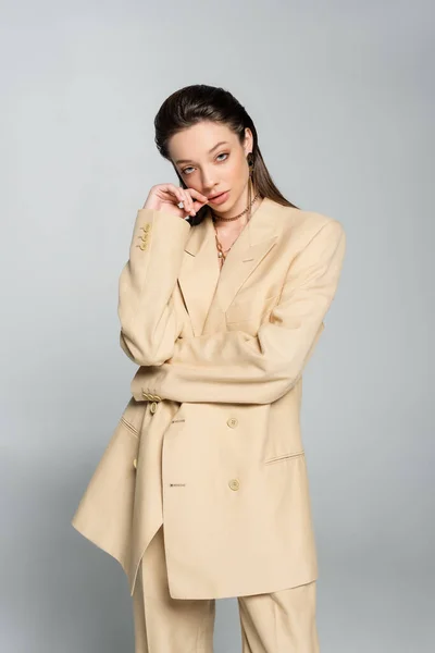 Pretty young woman in beige blazer looking at camera and posing on grey — Stockfoto