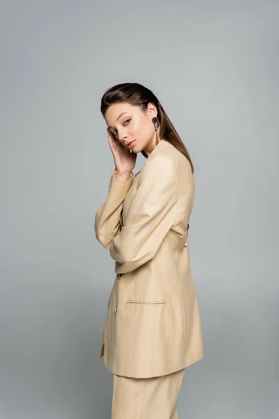 Brunette model in beige blazer looking at camera while posing isolated on grey — Foto stock
