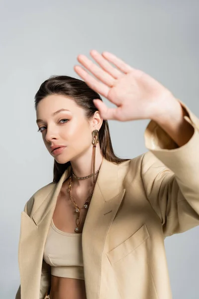 Pretty young woman in beige blazer looking at camera while gesturing isolated on grey - foto de stock