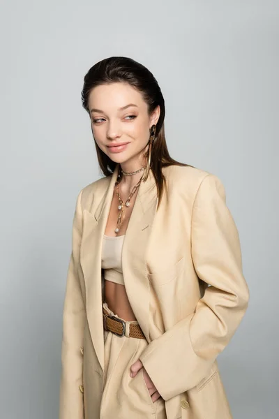 Cheerful young woman in stylish outfit posing with hand in pocket isolated on grey - foto de stock