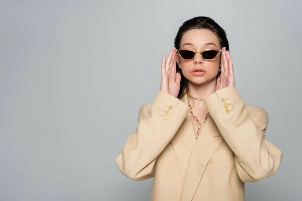 Young woman in stylish outfit wearing trendy sunglasses isolated on grey — стоковое фото