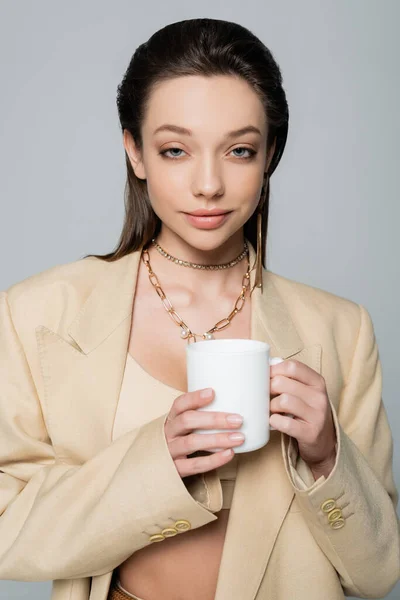 Smiling woman in stylish beige suit holding cup of coffee isolated on grey — Stock Photo