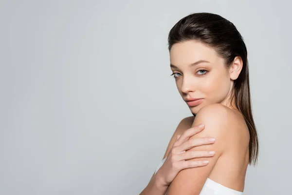Portrait of pretty young woman with bare shoulders and makeup looking at camera isolated on grey - foto de stock