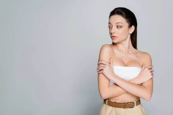 Pretty young woman with bare shoulders and makeup looking away isolated on grey — стоковое фото