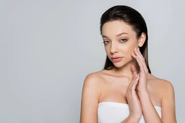 Portrait of brunette woman with bare shoulders and makeup looking at camera isolated on grey — Stockfoto