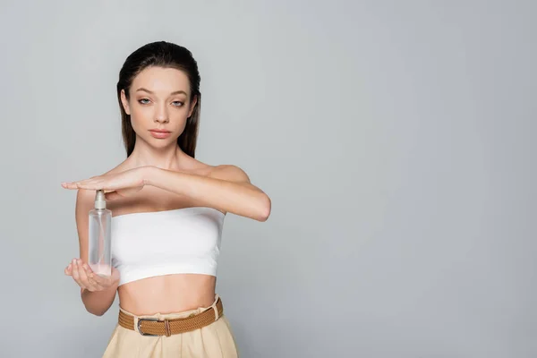 Young woman with bare shoulders holding spray bottle with thermal water isolated on grey - foto de stock