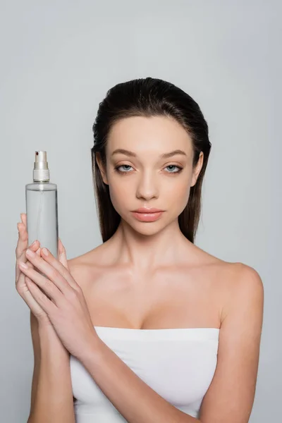 Young woman with bare shoulders holding bottle with thermal water isolated on grey — Fotografia de Stock