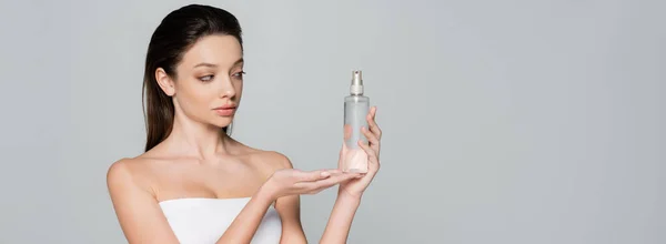 Young woman with bare shoulders holding bottle with cosmetic product isolated on grey, banner — Photo de stock
