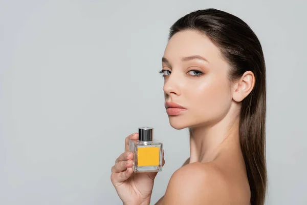 Young woman with bare shoulder holding bottle with perfume isolated on grey — Stock Photo