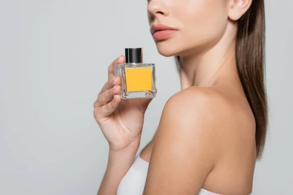 Cropped view of woman with bare shoulder holding bottle with perfume isolated on grey — Photo de stock