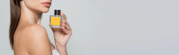 Cropped view of woman with bare shoulder holding bottle with perfume isolated on grey, banner — Foto stock