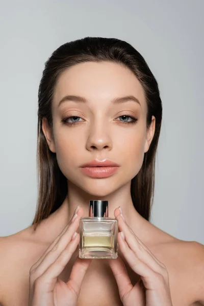 Young woman with blue eyes holding bottle with luxury perfume isolated on grey — стоковое фото