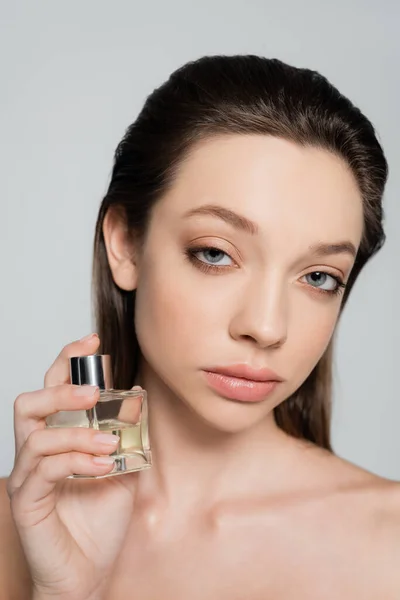 Portrait of young woman with blue eyes holding bottle with perfume isolated on grey — стоковое фото