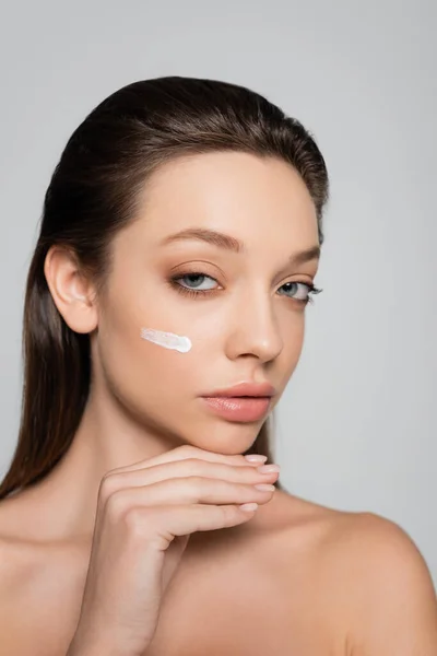 Young woman with bare shoulders and cream on face looking at camera isolated on grey — Stockfoto