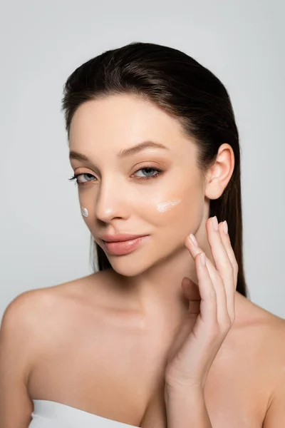 Young woman with bare shoulders and cream on cheeks smiling isolated on grey — Photo de stock