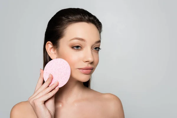 Young woman with bare shoulders holding exfoliating sponge isolated on grey - foto de stock