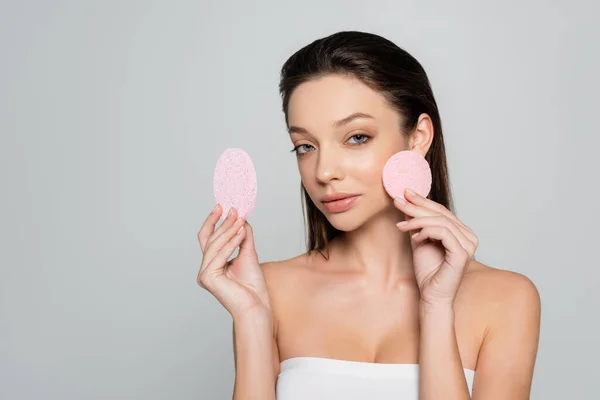 Young woman with bare shoulders holding exfoliating sponges isolated on grey — Foto stock