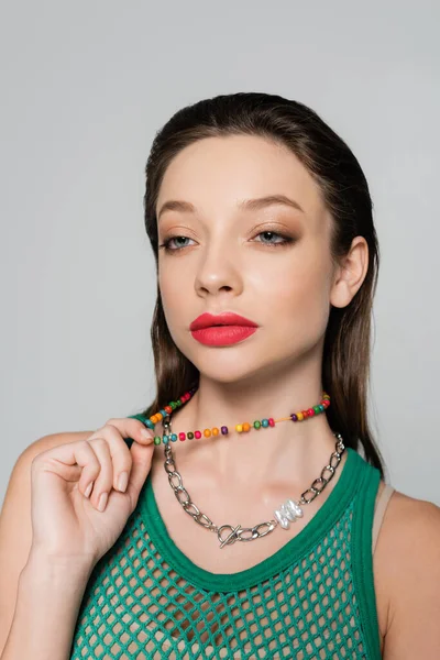 Stylish model with red lips pulling beads necklace isolated on grey — стоковое фото