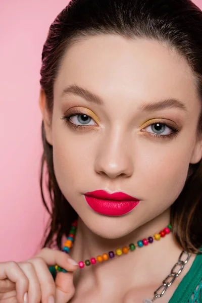 Close up view of young model with bright makeup posing while pulling beads necklace isolated on pink - foto de stock