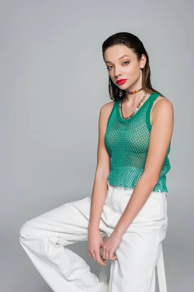 Stylish woman in green trendy outfit sitting on high chair isolated on grey — стоковое фото