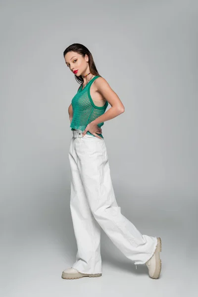 Full length of young woman in stylish outfit posing with hand on hip on grey — Stock Photo