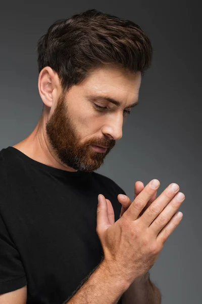 Portrait of bearded man in black t-shirt praying isolated on grey — Stock Photo