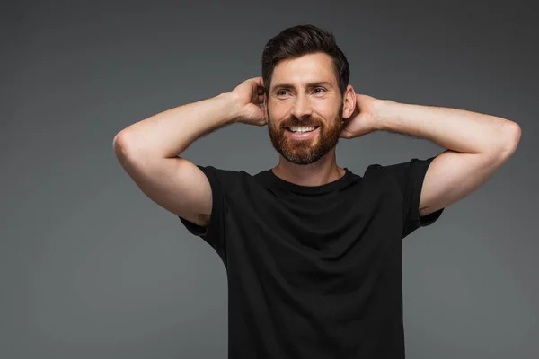 Portrait of cheerful man in black t-shirt posing with hands behind head isolated on grey — Stockfoto
