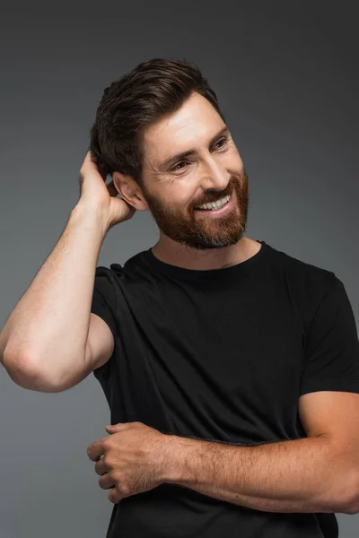 Portrait of pleased man in black t-shirt looking at camera isolated on grey — Stockfoto