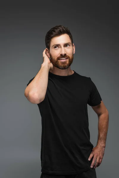 Portrait of smiling bearded man in black t-shirt looking away isolated on grey - foto de stock