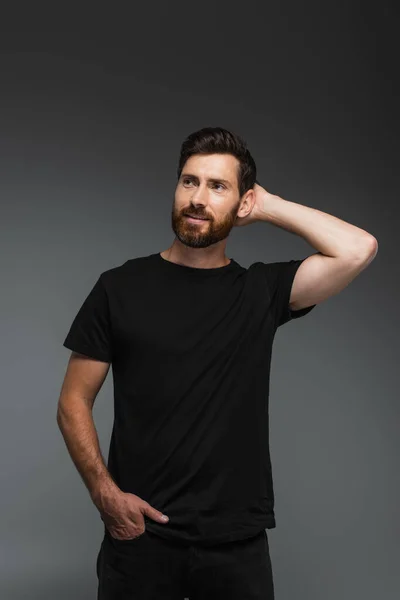 Portrait of cheerful man in black t-shirt posing with hand in pocket isolated on grey — Stock Photo