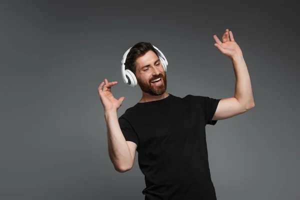 Happy bearded man in wireless headphones listening music isolated on grey — Photo de stock