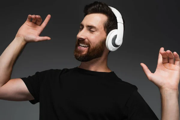 Bearded man in wireless headphones listening music isolated on grey — Fotografia de Stock