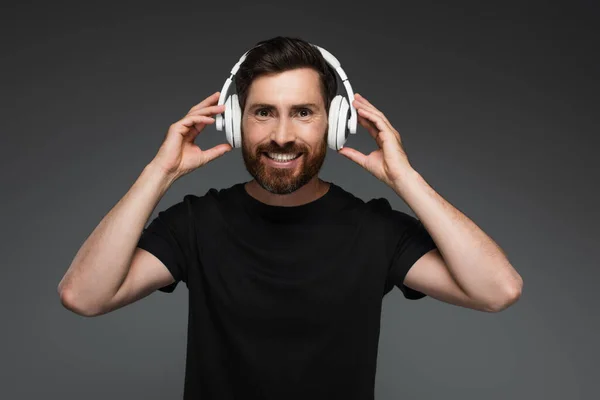 Веселий і бородатий чоловік у бездротових навушниках слухає музику ізольовано на сірому — стокове фото