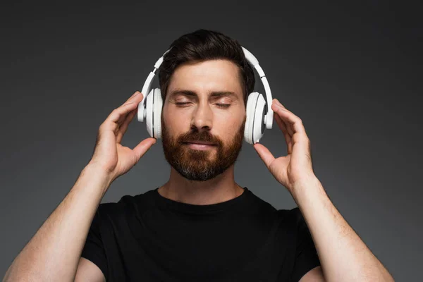 Бородатый человек в беспроводных наушниках слушать музыку изолированы на серый — стоковое фото