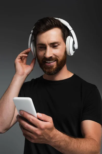 Радісна людина в бездротових навушниках слухає музику і використовує смартфон ізольовано на сірому — стокове фото