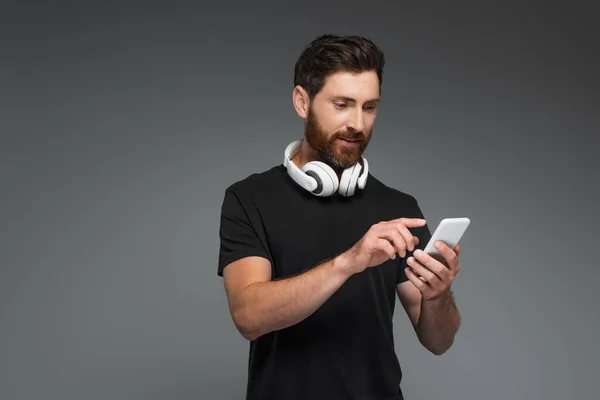 Cheerful man in wireless headphones using smartphone isolated on grey — Foto stock
