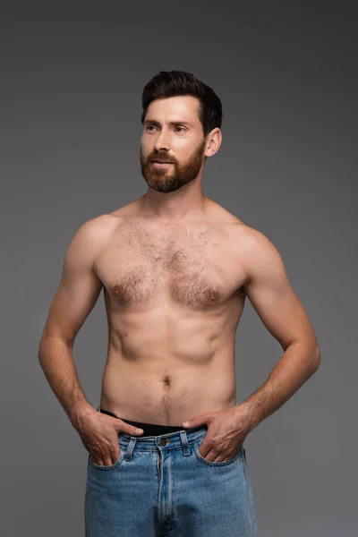 Shirtless and bearded man with hair on chest posing with hands in pockets isolated on grey - foto de stock