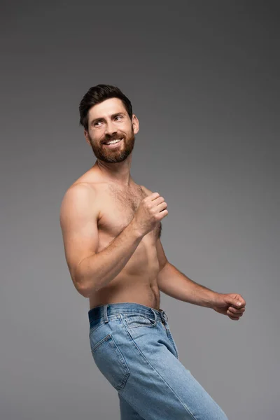 Positive and shirtless man with beard standing in denim jeans isolated on grey — Fotografia de Stock