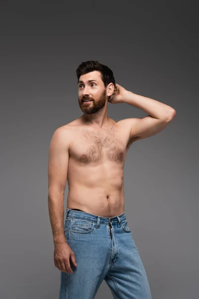 Puzzled and shirtless man with beard standing in denim jeans isolated on grey — Fotografia de Stock